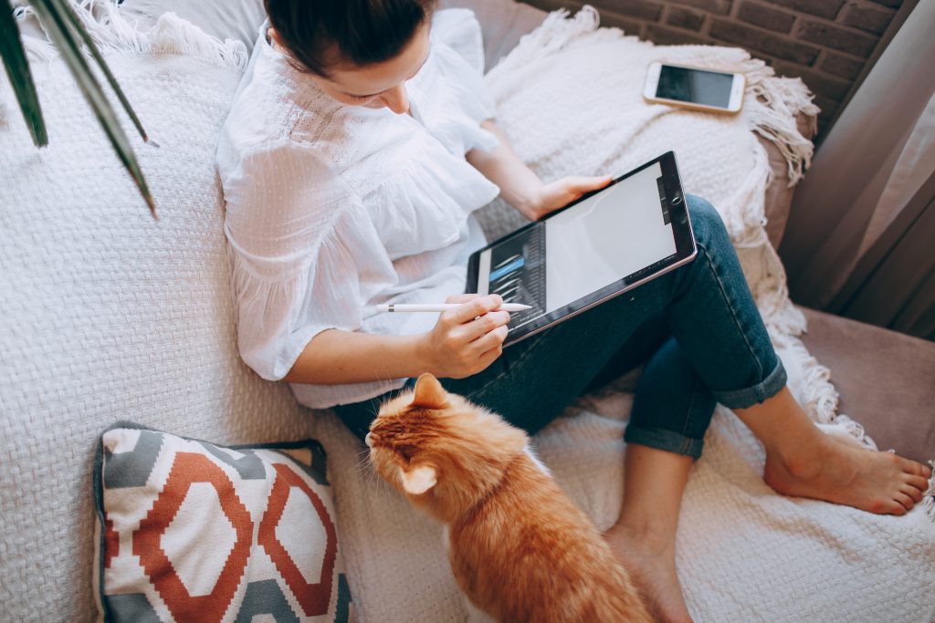 a woman with a tablet on a couch with a cat